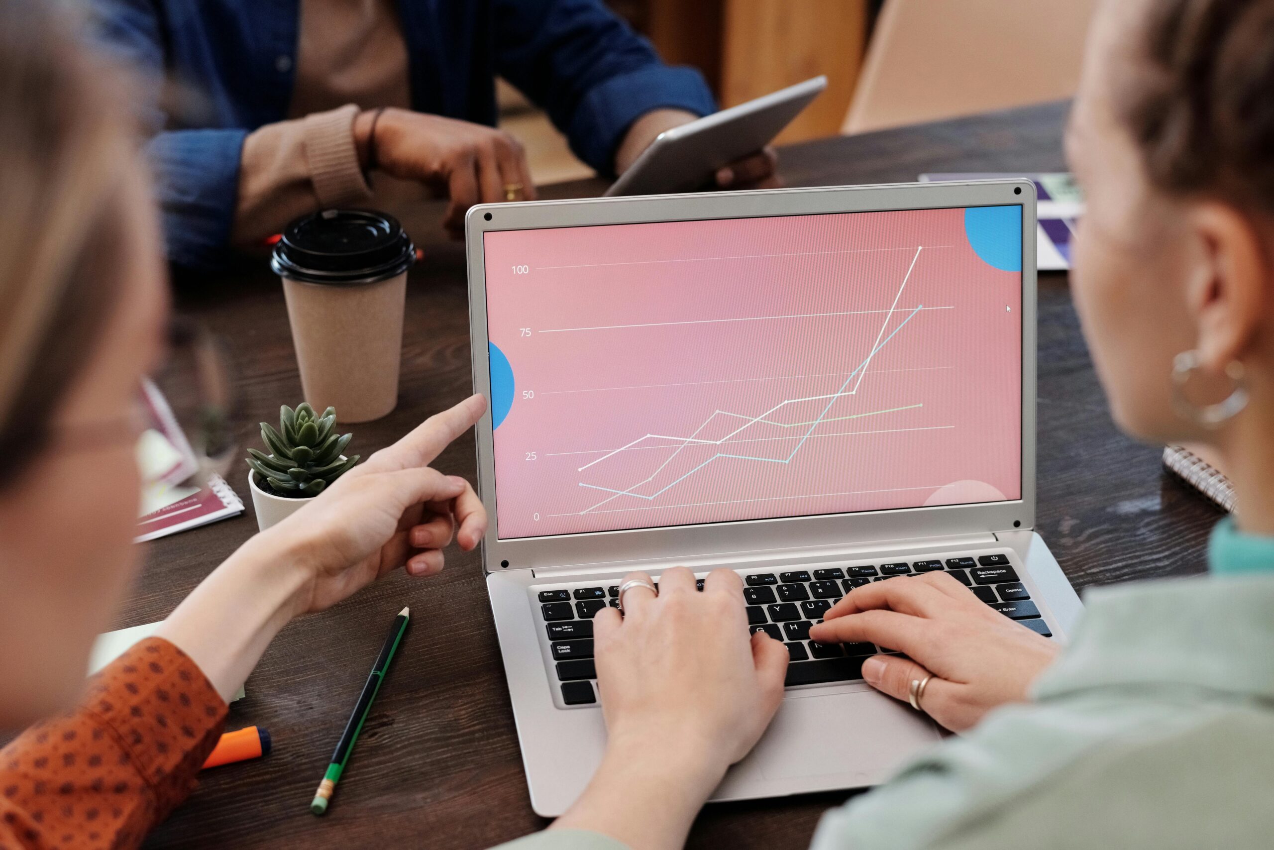 Office workers collaboratively reviewing data trends on a laptop during a meeting.